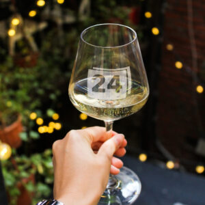 Weißweinglas mit Gravur „24“, in Hand gehalten mit Lichterkette